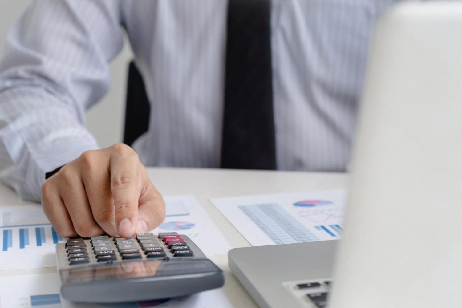Auditor using a calculator and laptop while reviewing financial charts during a company risk audit